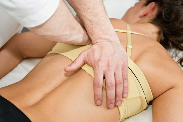 A physical therapist assisting a middle-aged man with back stretches in a bright clinic room.