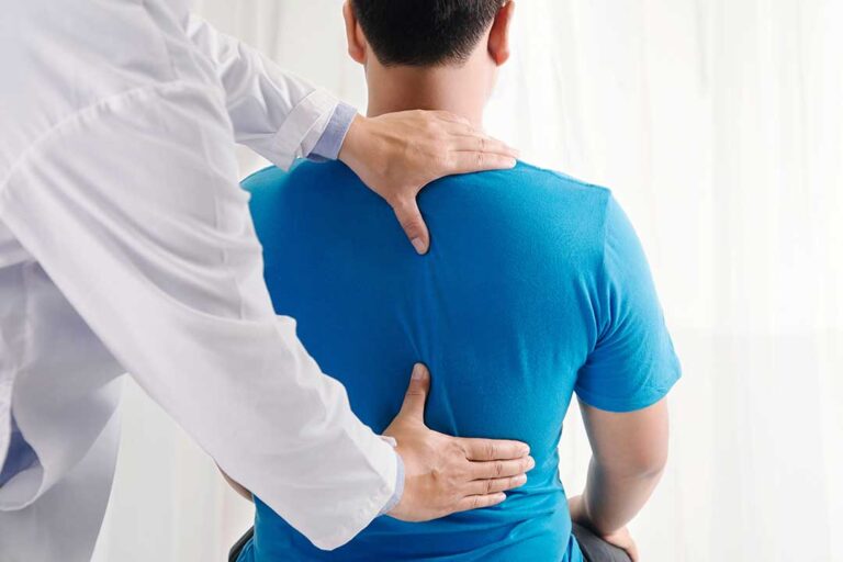 Adult seated during a balance assessment while a clinician observes head and eye movement.