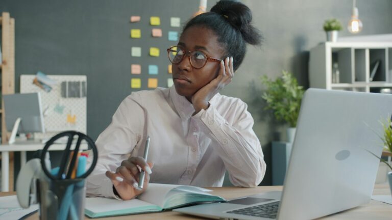 Person seated at a desk gently touching a sore jaw while maintaining relaxed neck and shoulder posture.